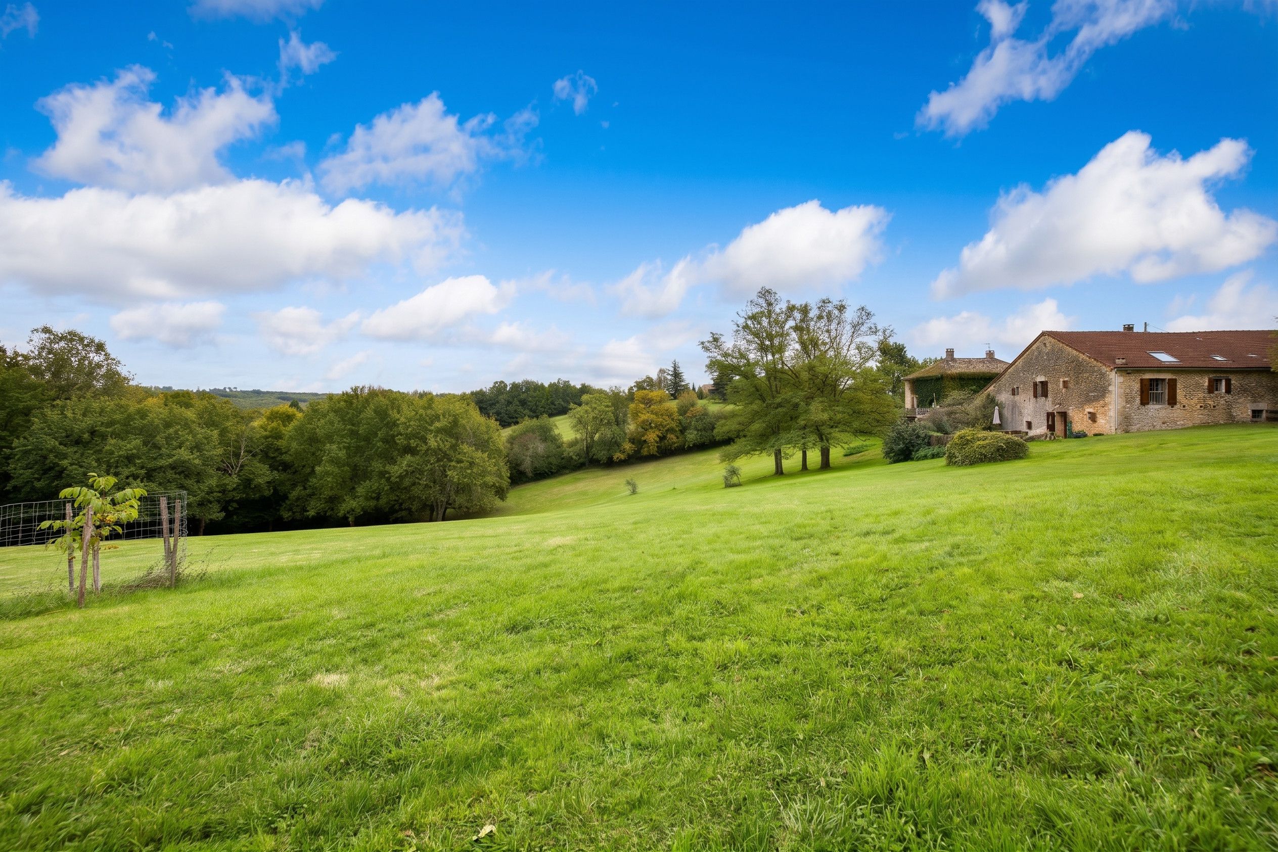 A rural landscape with a stone house on a hillside, surrounded by lush green fields and trees.