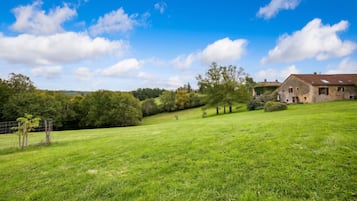 A rural landscape with a stone house on a hillside, surrounded by lush green fields and trees.