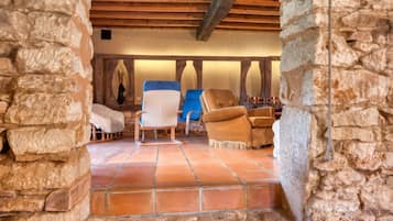 A stone-walled room with a wooden ceiling, a tiled floor, and two upholstered chairs.