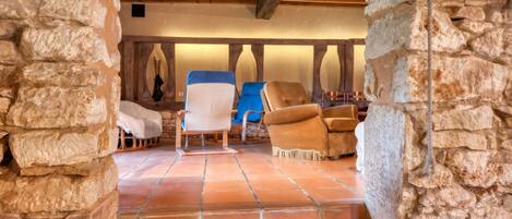 Una habitación con paredes de piedra, techo de madera y suelo de baldosas, con dos sillones tapizados.