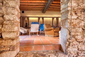 Una habitación con paredes de piedra, techo de madera y suelo de baldosas, con dos sillones tapizados.