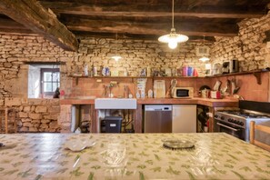 Une cuisine rustique avec des murs en pierre, des poutres en bois, un pare-feu en carreaux et divers appareils de cuisine.