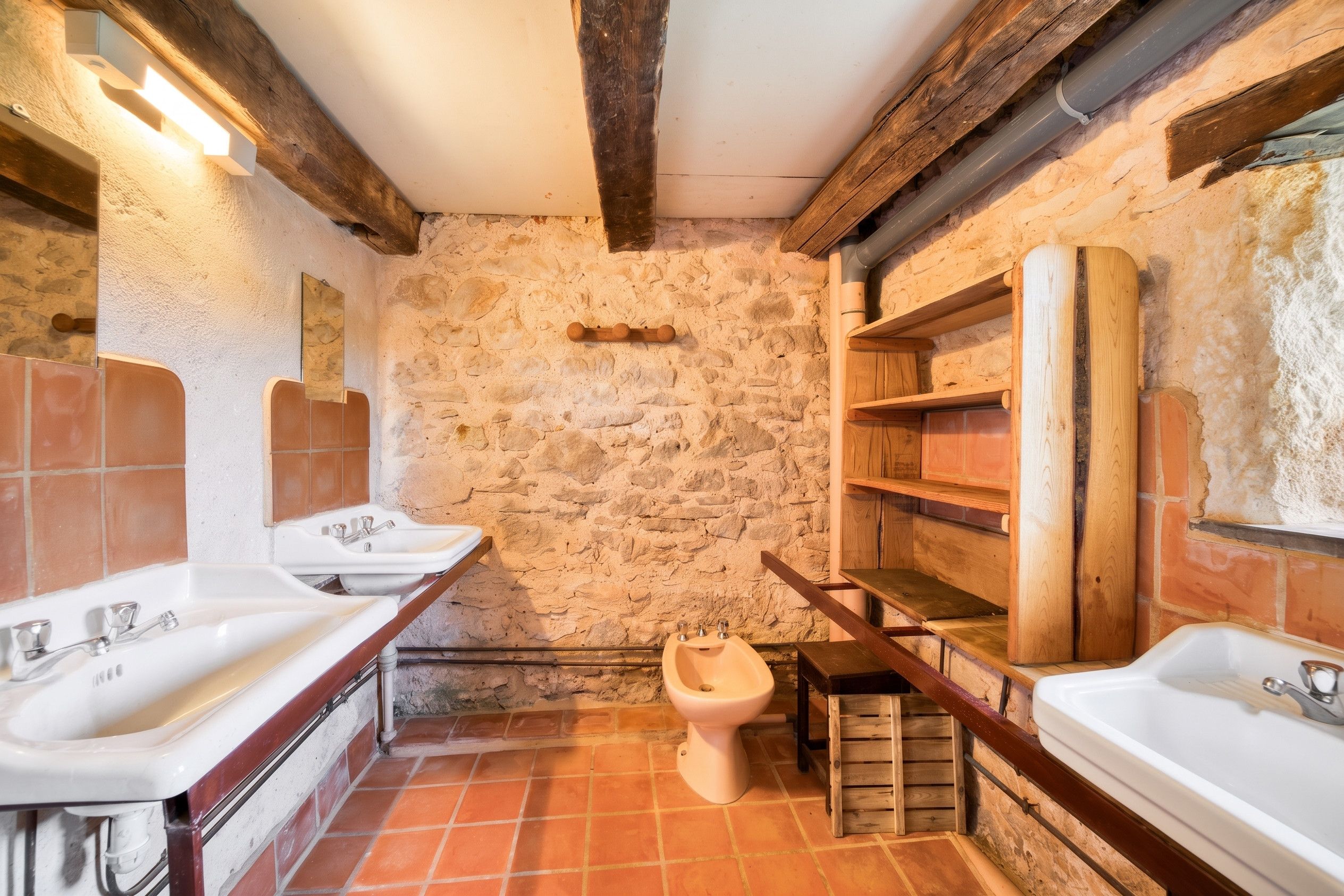 Un baño rústico con paredes de piedra, vigas de madera y un inodoro.