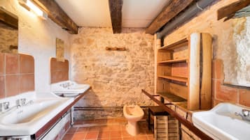 Un baño rústico con paredes de piedra, vigas de madera y un inodoro.