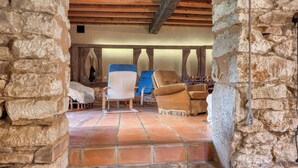 Una habitación de paredes de piedra con suelo de baldosas, vigas de madera y dos sillas.