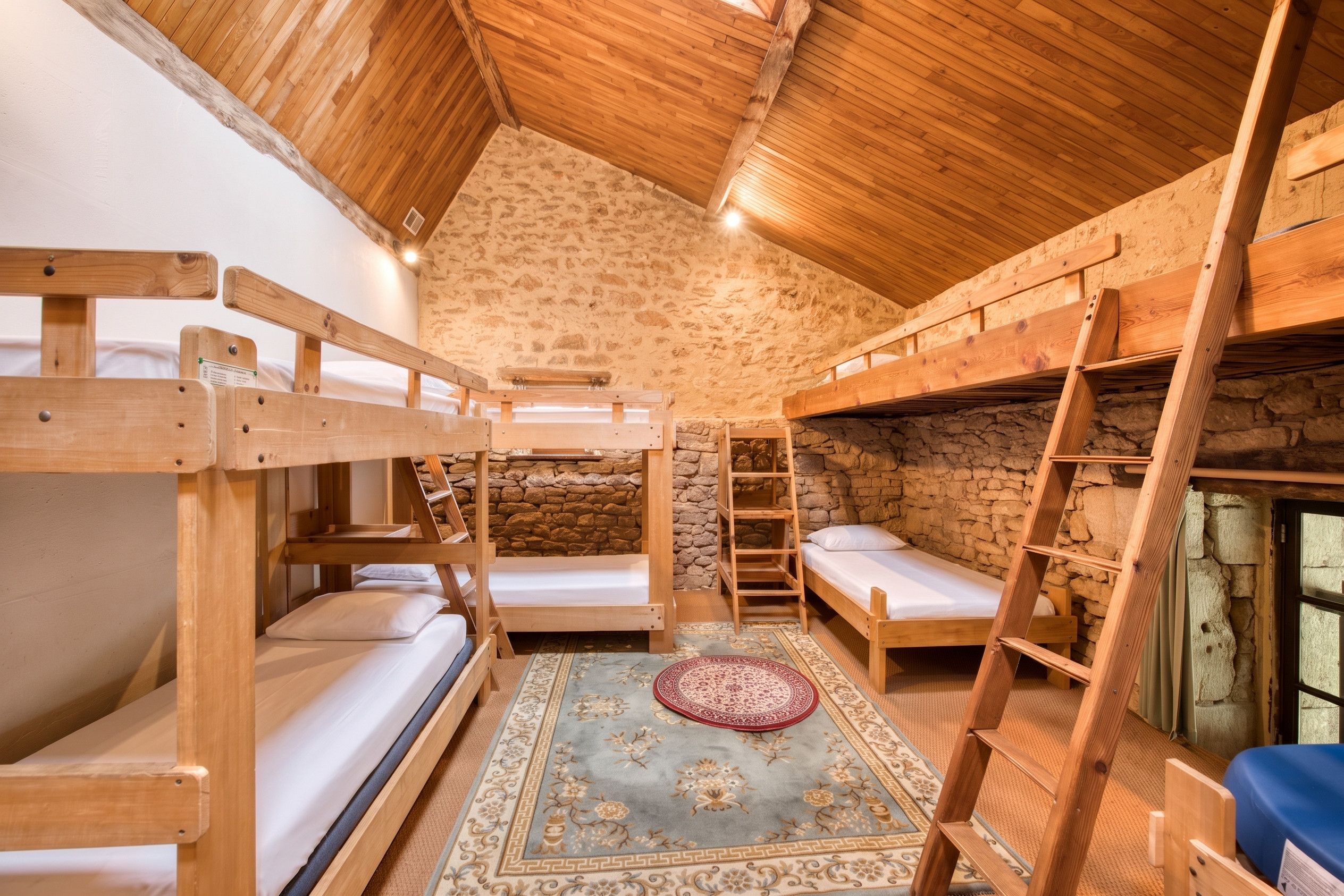 A rustic wooden room with bunk beds, a stone wall, and a ladder.