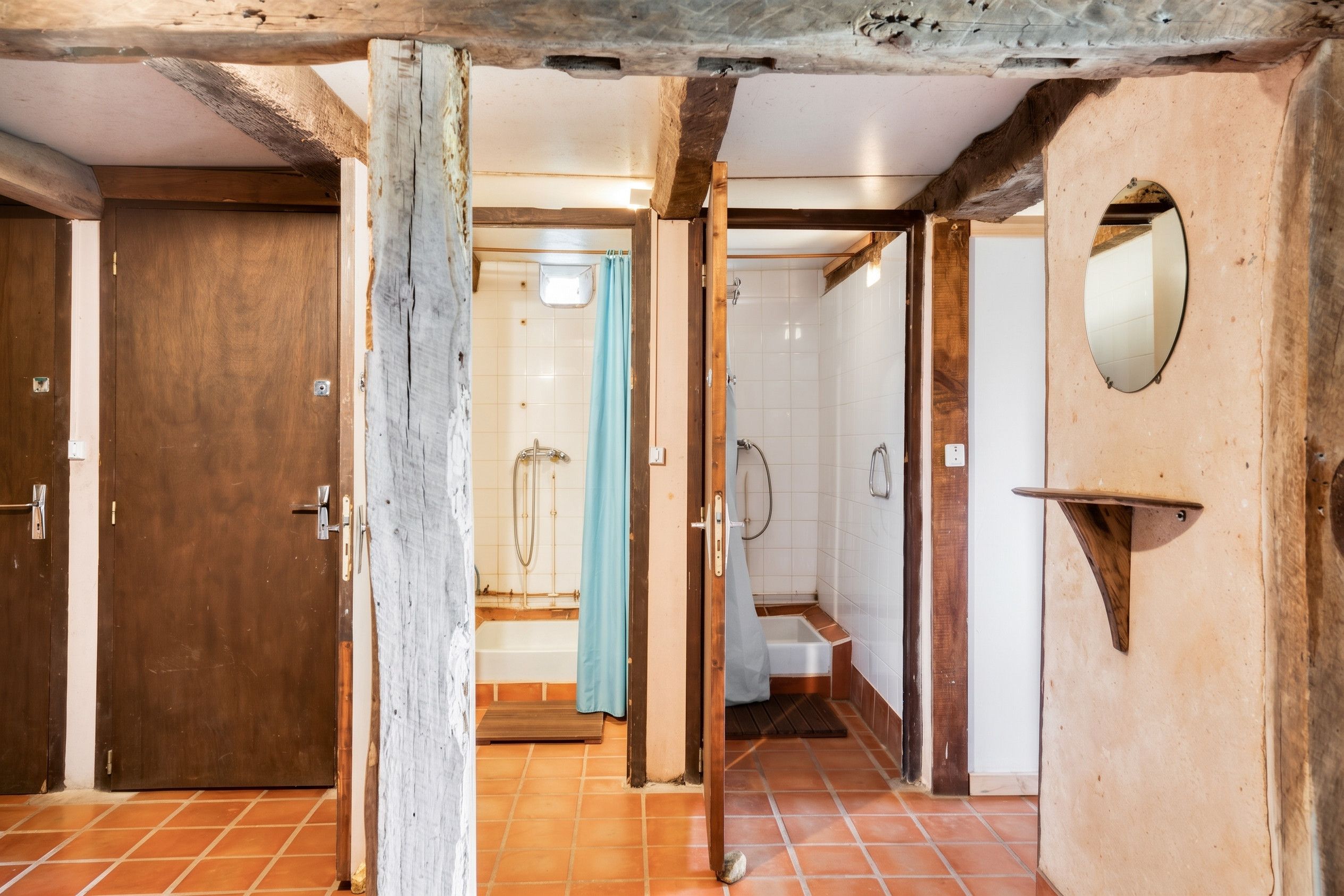Un couloir avec une porte en bois, une salle de bain avec douche et des toilettes.