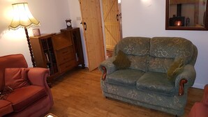 A cozy living room with a wooden floor, a green patterned sofa, a red armchair, a wooden cabinet, and a lamp. - Beautiful 2 bedroomed stone cottage in the centre of Crich  (Crich)