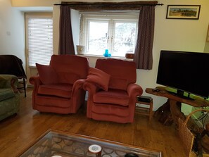 Un salon avec deux fauteuils rouges, un fauteuil vert, un téléviseur et une fenêtre avec des rideaux.