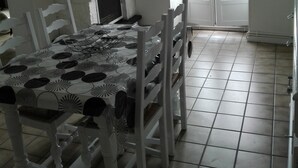 A dining area with a table set for four, white chairs, a black and white patterned tablecloth, a white ceiling, and a view through a glass door to the outside.