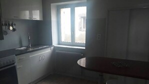 A kitchen with a stove, sink, and window. There is a table with two stools.