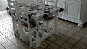 A dining area with a white table and chairs, a tiled floor, and a white cabinet with a picture on top.