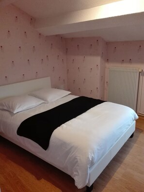 A bedroom with a bed, white bedding, a black throw blanket, and a radiator.
