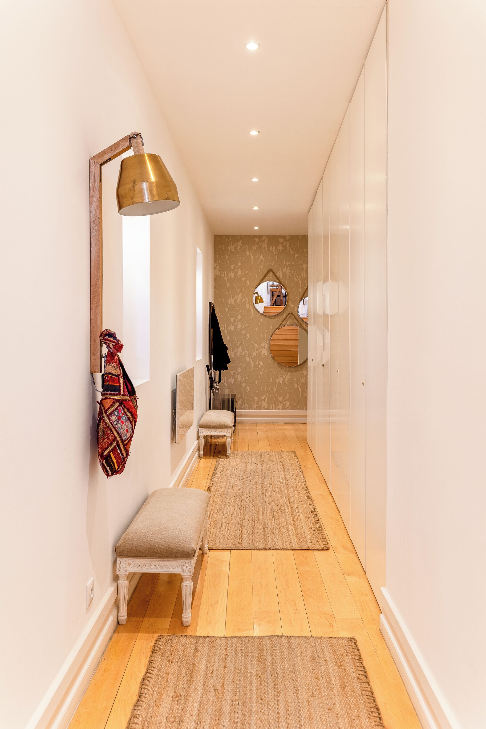 A hallway with a bench, a wall-mounted lamp, and a mirror.