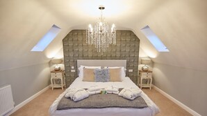 Quarto com cama grande, duas mesas de cabeceira, um candelabro e teto inclinado com claraboias.