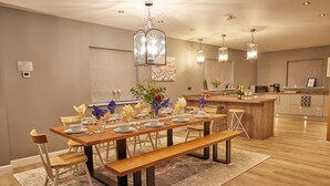 Uma sala de jantar moderna com uma mesa de madeira para seis pessoas, bancos e uma cozinha ao fundo.