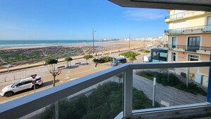 A balcony with a view of a beach, a parked car, and a building labeled 'PIZZERIA' in the background.