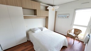 A bedroom with a bed, wooden wardrobe, and a chair by a window.