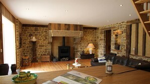 A rustic room with a stone wall, a fireplace, a sofa, and a wooden table with a brochure. - Charming house with garden and parking in Val-Saint-Père (Le Val-Saint-Père)