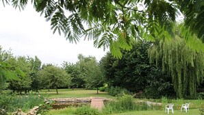 A serene garden with a pond, lush greenery, and a seating area with chairs. - Charming house with garden and parking in Val-Saint-Père (Le Val-Saint-Père)