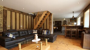 A cozy living room with a black leather sofa, a glass coffee table, and a wooden staircase. - Charming house with garden and parking in Val-Saint-Père (Le Val-Saint-Père)