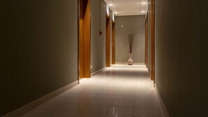 Un pasillo largo, bien iluminado, con puertas de madera y suelo de baldosas.