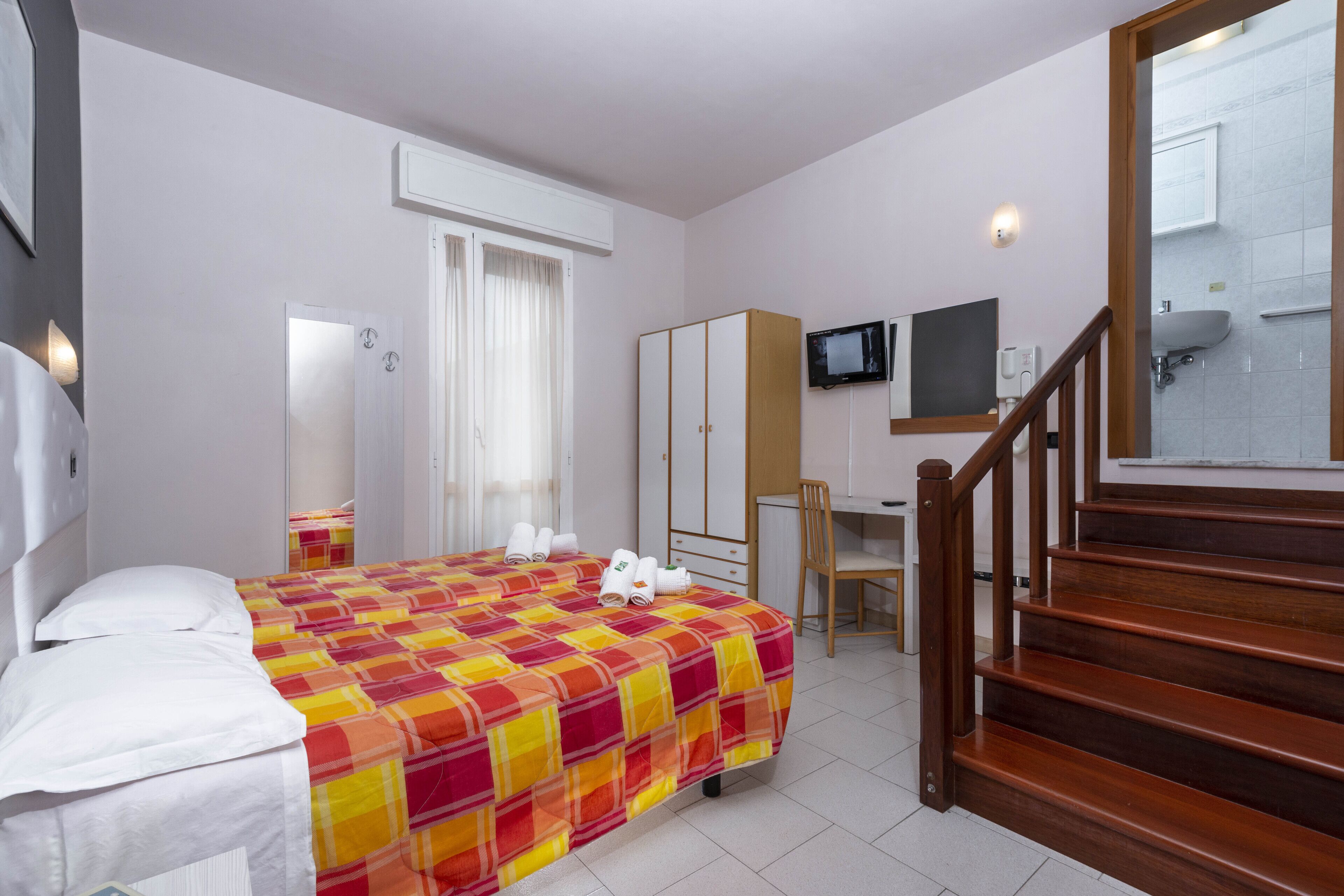A hotel room with a bed, a desk, a chair, a television, and a staircase.