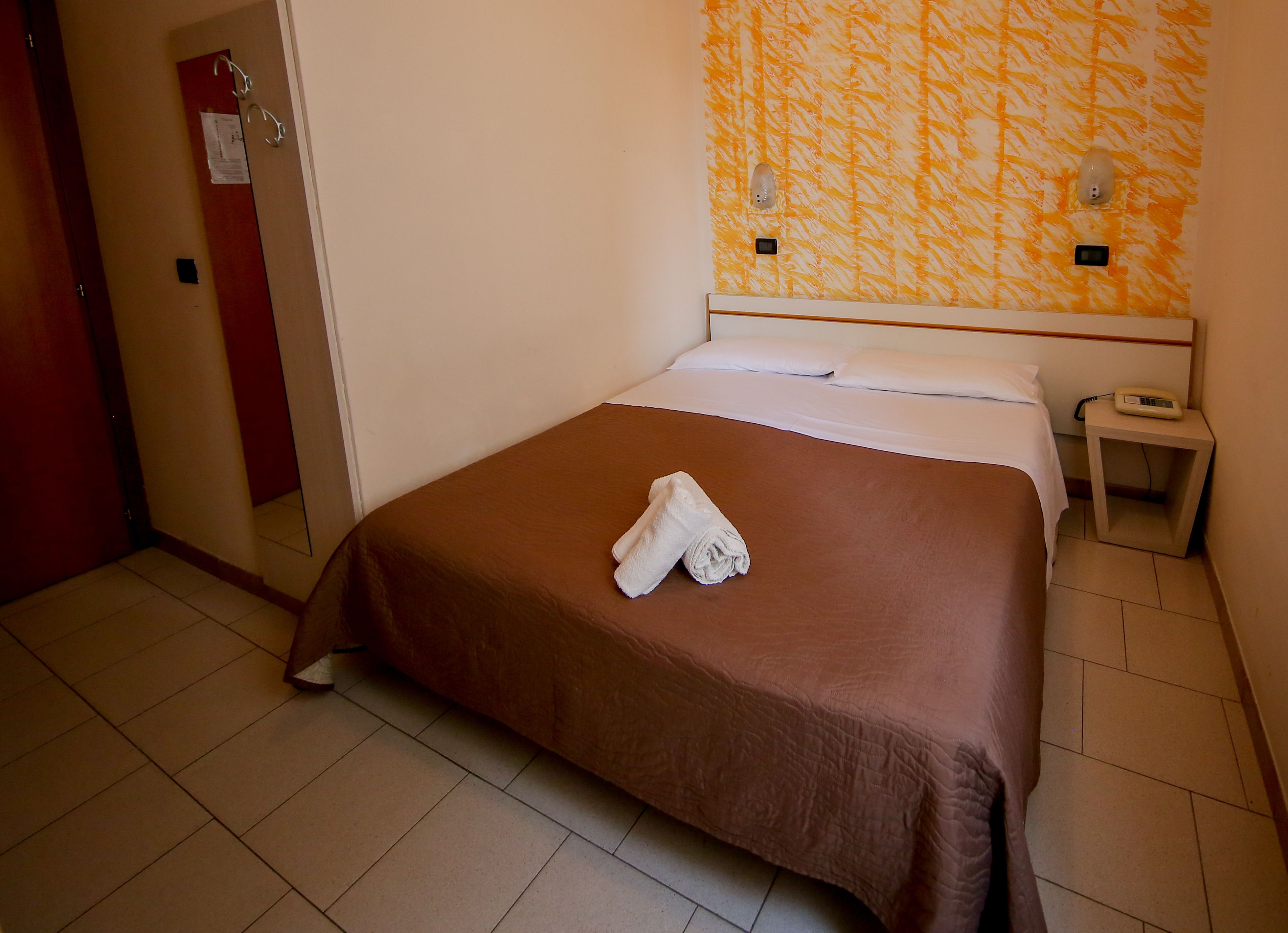 A hotel room with a bed, a nightstand, and a wall with a patterned design.