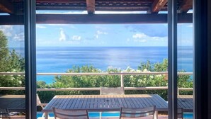 A patio with a table and chairs, a pool, and a view of the ocean.