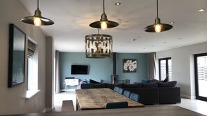 A modern living room with a large wooden dining table, dark sofas, and pendant lighting. - Wild Cherry Barn, Ashlin Farm Barns (Lincoln)