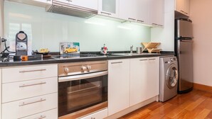 Una cuina moderna amb armaris blancs, un frigorífic d'acer inoxidable, un forn integrat i una rentadora.