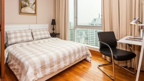 Habitació d'hotel amb un llit, una taula, una cadira, una làmpada i una finestra gran amb vista a la ciutat.