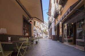 A narrow street with outdoor seating, buildings on either side, and a clear sky.