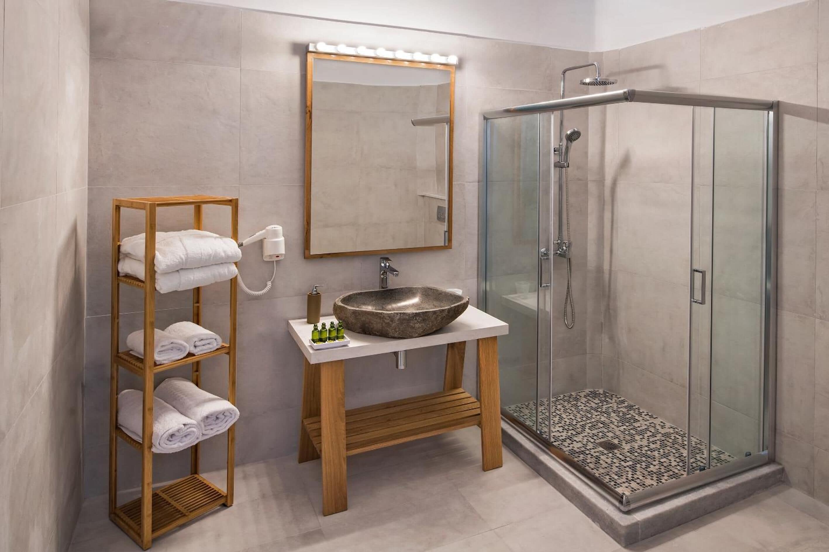 A modern bathroom with a glass shower enclosure, a wooden towel rack, a large mirror, and a stone sink.