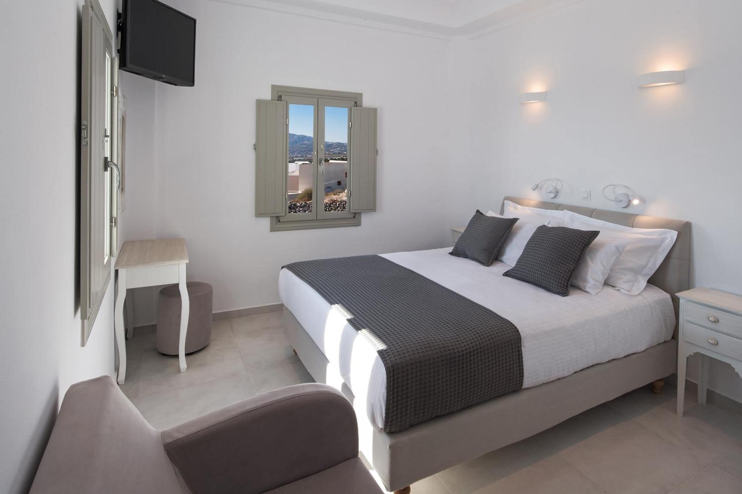 A bedroom with a bed, bedside tables, a chair, a TV mounted on the wall, and a window with a view.