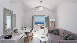 Un espace de vie compact comprenant un coin cuisine, un coin repas et un coin salon. Il dispose d’une grande fenêtre offrant une vue sur la mer.