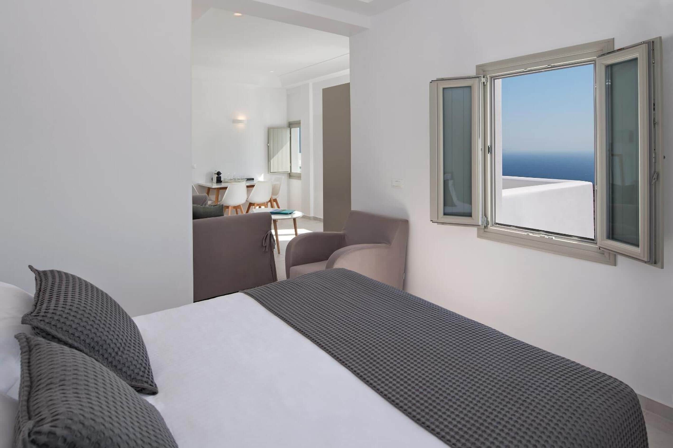 Quarto de hotel com cama, janela com vista para o mar, pequena área de refeições e banheiro.