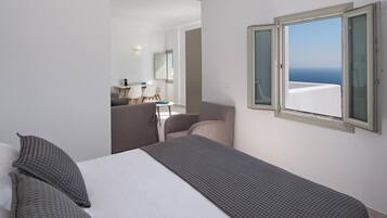 Quarto de hotel com cama, janela com vista para o mar, pequena área de refeições e banheiro.