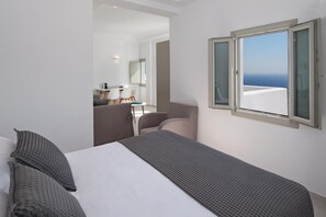 Quarto de hotel com cama, janela com vista para o mar, pequena área de refeições e banheiro.