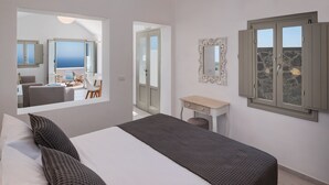 Une chambre à coucher avec un lit, une petite table de chevet, un miroir et une fenêtre donnant sur la mer.