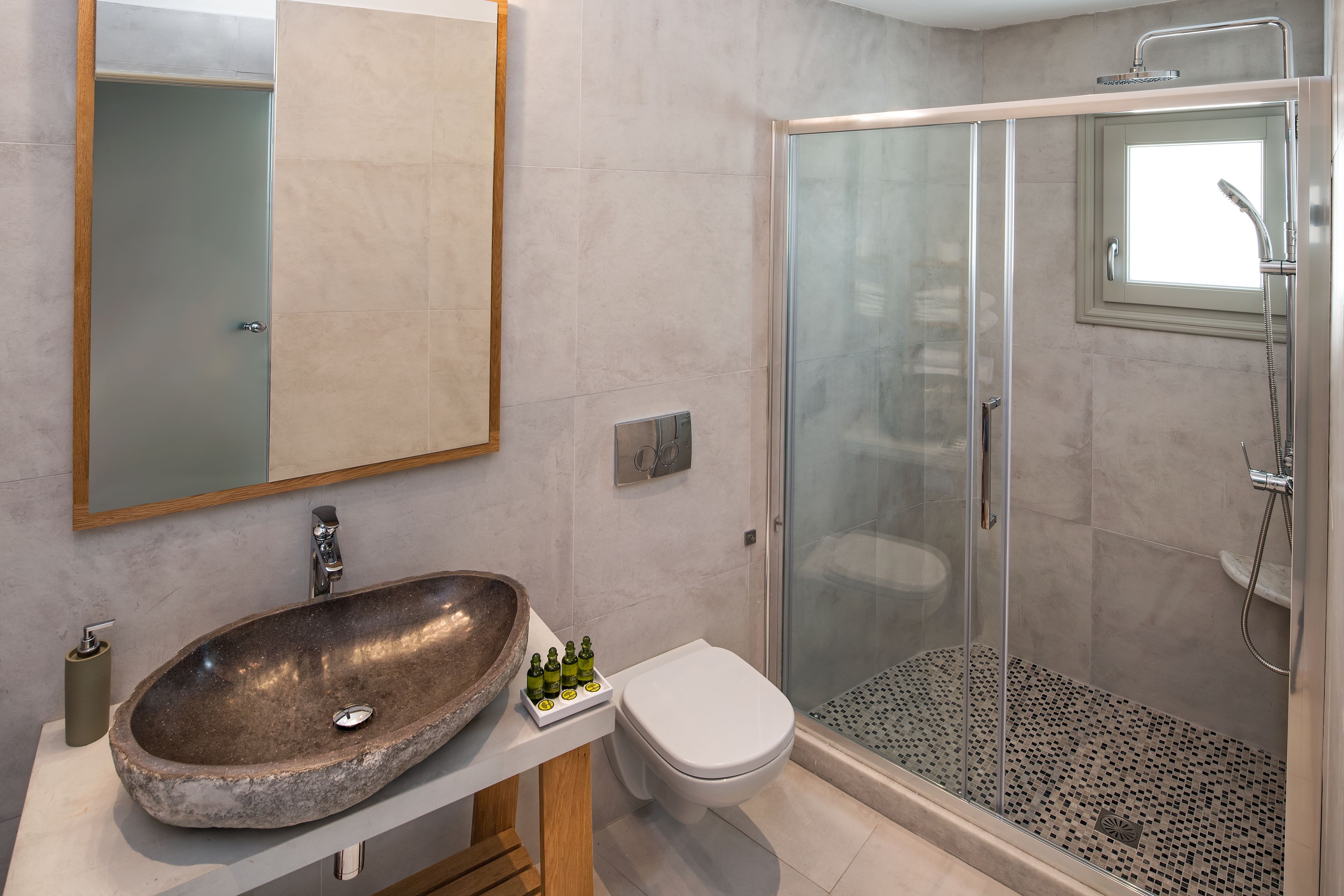 A modern bathroom with a stone sink, a toilet, and a glass-enclosed shower.
