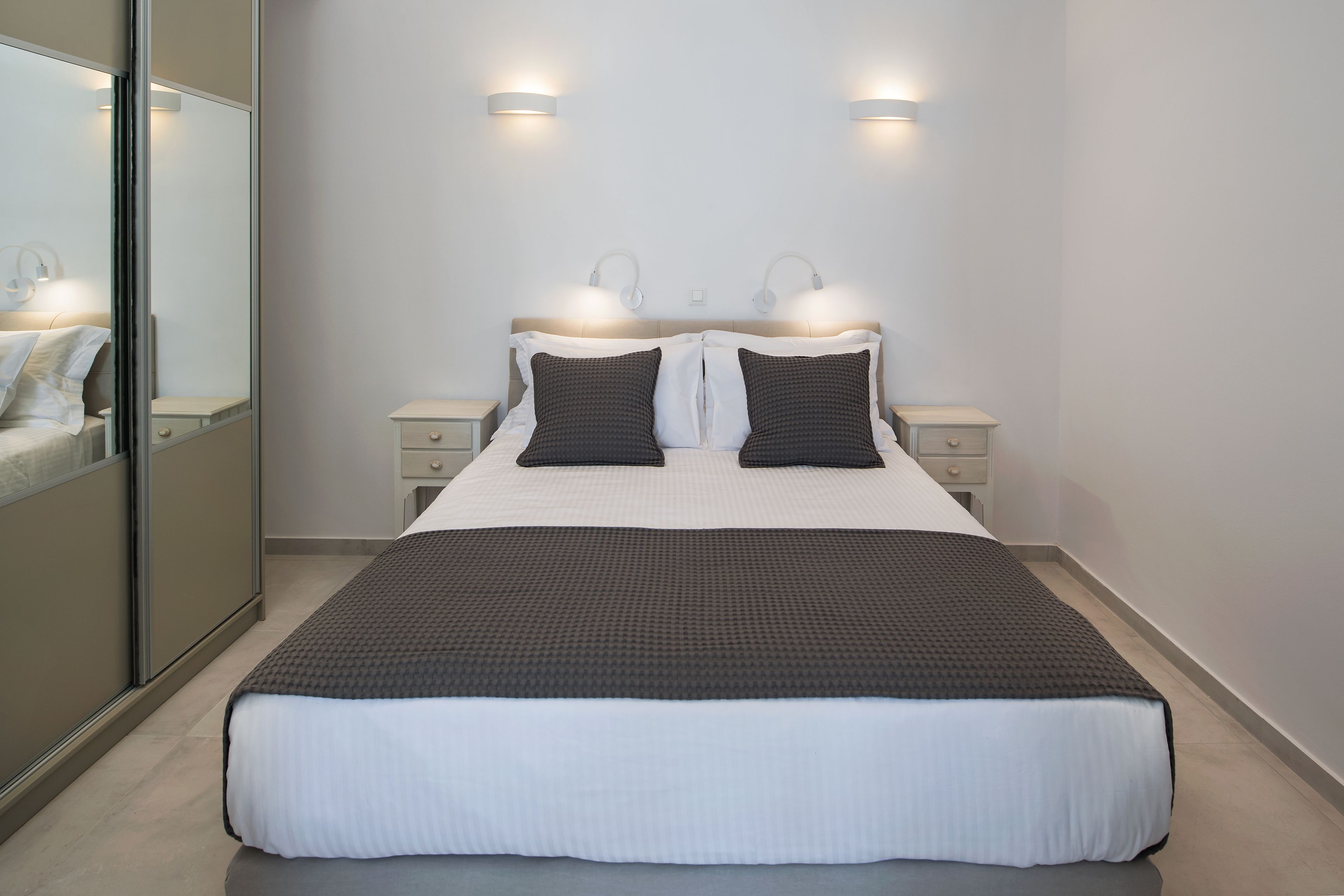 A modern bedroom with a large bed, two bedside tables, and wall-mounted lighting.