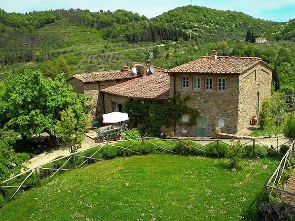 A stone house with a tiled roof, surrounded by a grassy yard and trees.