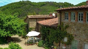 A stone building with a tiled roof, a gravel courtyard, and a table with chairs under a white umbrella. - A luxury escape in Chianti, great landscape, stunning views, swimming pool (San Polo in Chianti)