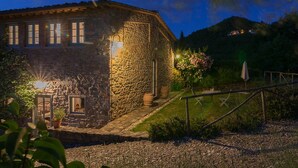 A stone building with a well-lit entrance and a small garden area. - A luxury escape in Chianti, great landscape, stunning views, swimming pool (San Polo in Chianti)