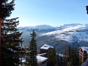 Ein Berggasthof mit schneebedeckten Dächern, umgeben von immergrünen Bäumen und Blick auf verschneite Berge.