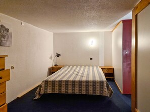 Quarto com cama, mesa de cabeceira, luminária, cômoda e porta.
