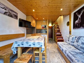 Um interior acolhedor com uma mesa de jantar de madeira, um sofá e uma escada que leva a um andar superior.