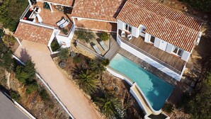 An aerial view of a property with a swimming pool, multiple terraces, and a paved driveway.
