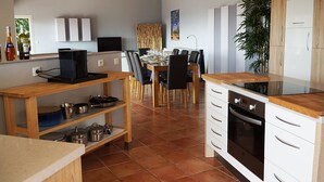 A modern kitchen with a dining area, featuring a wooden table, chairs, a built-in oven, and a TV on a shelf.